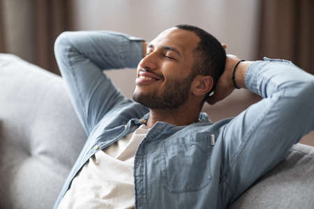 Domestic Comfort. Relaxed Young Black Man Leaning Back On Couch At Homeの写真素材