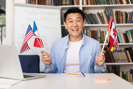 Asian Language Teacher Man Holding Different Countries Flags Sitting Indoorの写真素材