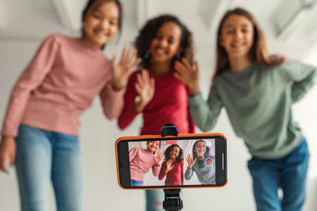 Three Girls Waving To Phone Making Video For Blog Indoorsの写真素材