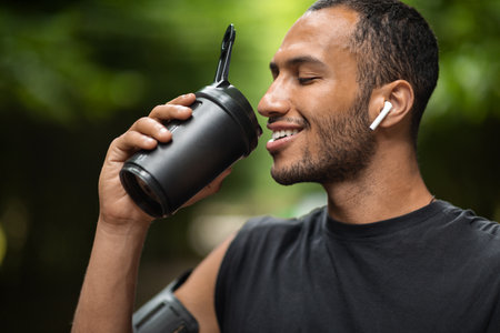Closeup of handsome black man drinking protein cocktail, training outdoorsの写真素材