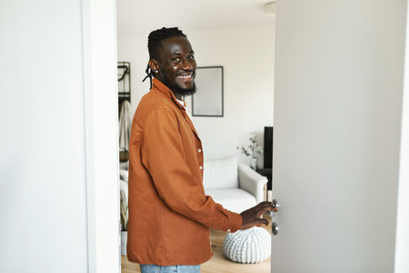 Welcome to my home. Cheerful black man walking in his apartment, entering new home and looking back...
