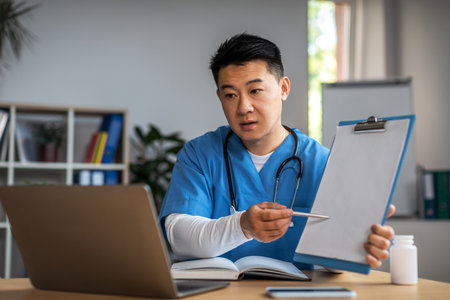 Serious mature asian man doctor show tablet to laptop in clinic office interior. Video call, treatment with therapistの写真素材