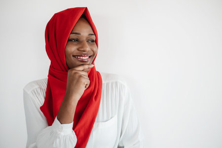 Nice offer. Curious black muslim woman looking away at free space and touching chin, posing on light backgroundの写真素材