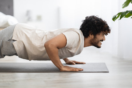 Positive young eastern man exercising on fitness mat at home