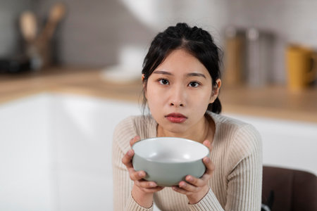 Starving asian woman holding empty plate next to mouthの写真素材