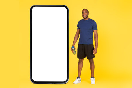Sporty Black Male Posing Near Phone Large Screen, Yellow Backgroundの写真素材