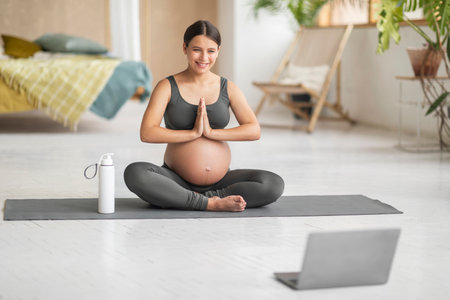 Beautiful Pregnant Woman Having Online Yoga Lesson With Laptop At Homeの写真素材