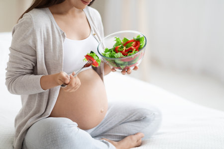 Cropped of pregnant woman eating healthy vegetable salad, bedroom interiorの写真素材