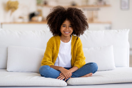 Cheerful african american girl sitting on couch at homeの写真素材