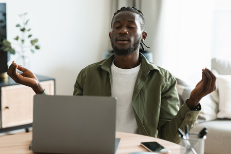 Relaxed african american male freelancer meditating, working at laptop, calming down, sitting with closed eyesの写真素材