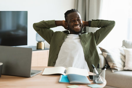 Portrait of excited black businessman relaxing on chair, leaning back, holding hands behind head and smilingの写真素材