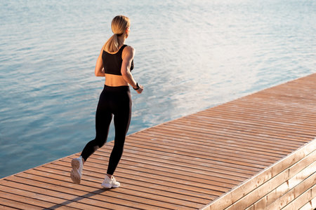 Sporty Woman In Activewear Running Outdoors On Wooden Pier Near Riverの写真素材