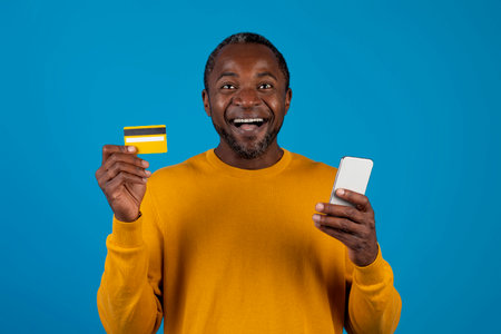 Excited black man holding cell phone and credit cardの写真素材