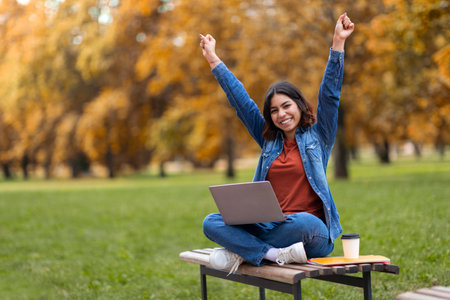 Joyful Arab Female Student Siting Outdoors With Laptop And Celebrating Successの写真素材