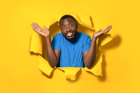I dont know. African american man shrugging shoulders and spreading arms, standing in torn yellow...