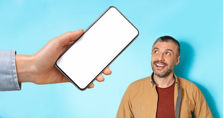 Happy inspired senior european man looking at huge smartphone with empty screen in hand isolated on...