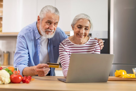 Senior Couple Ordering Groceries Online With Laptop And Credit Card In Kitchenの写真素材