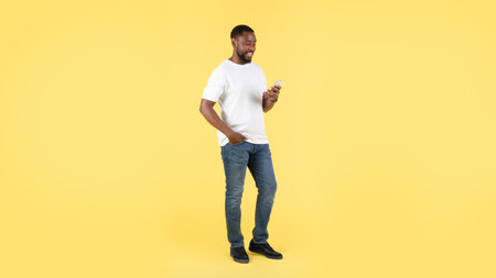 Happy Black Male Using Phone Standing Onr Yellow Background, Panoramaの写真素材