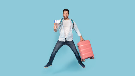 Excited happy millennial caucasian man with beard with suitcase and air tickets jumping in air