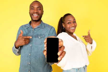 Cheerful African American Spouses Showing Smartphone Screen Over Yellow Backgroundの写真素材