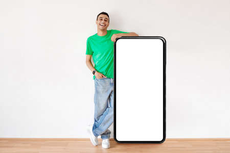 Positive arab man standing by big cellphone with white blank screen, recommending website or ad,...