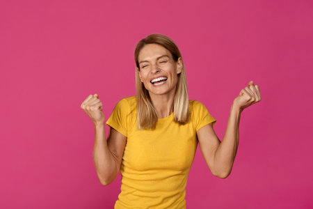 Cheerful adult european lady rejoices to victory and makes success gesture with handsの写真素材