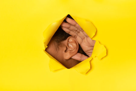 Unrecognizable African American Woman Putting Ear To Torn Yellow Paperの写真素材