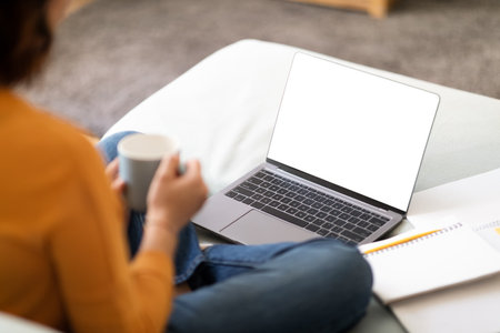 Unrecognizable Female Using Laptop With Blank White Screen And Drinking Coffeeの写真素材