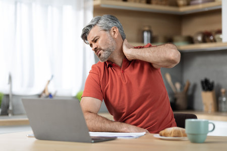 Tired man sitting in front of laptop, touching neck