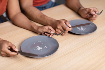 Hands of young black male and guy with forks and knives with plates of several grains of rice on wooden tableの写真素材