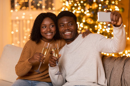 Glad millennial black couple cheers with glasses of champagne, man takes selfie on smartphoneの写真素材