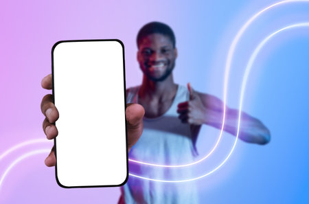 Positive black guy sportsman showing smartphone with empty screenの写真素材