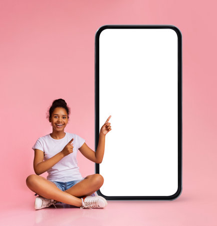 Mobile Ad. Cheerful Black Teen Girl Pointing At Big Blank Smartphone Screenの写真素材