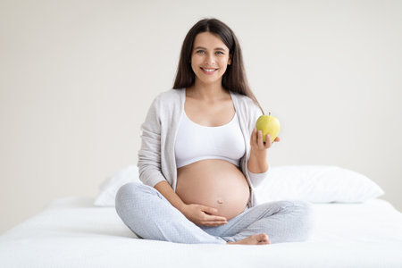 Happy pregnant woman holding apple and touching belly
