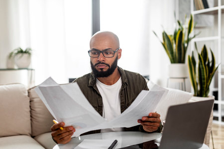 Concentrated mature latin male entrepreneur working with financial documents, checking annual...
