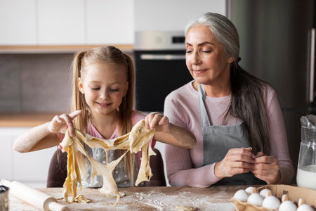 Cheerful caucasian little granddaughter and elderly grandmother make cookie dough, enjoy lessonの写真素材
