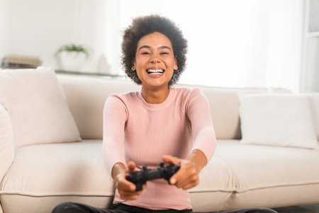 Happy excited millennial african american female with joystick, sit on floor, playing online gamesの写真素材