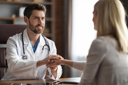 Smiling Male Doctor Holding Hand Of Female Patient During Meeting In Clinicの写真素材