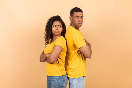 Frustrated african american spouses standing back to back with folded arms on peach studio...