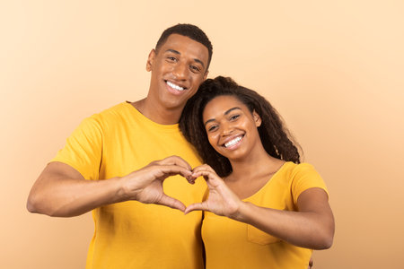 Loving african american couple cuddling and making together heart shape gesture with their hands as...