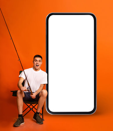 Excited Young Man With Fish-Rod Sitting Next To Big Blank Smartphone