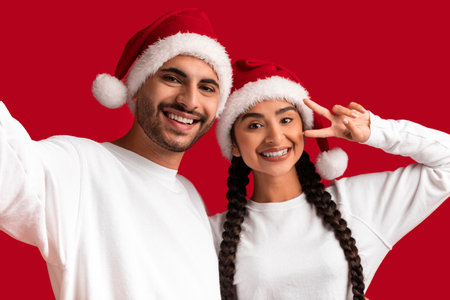 Happy Young Middle Eastern Couple In Santa Hats Taking Selfie Togetherの写真素材