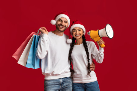 Holiday Sale. Arab Couple Wearing Santa Hats Holding Shopping Bags And Megaphone