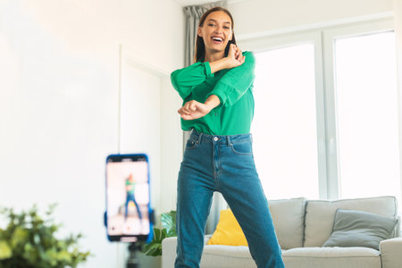 Playful young woman dancing making video for blog, having fun at home, lady using smartphone on...