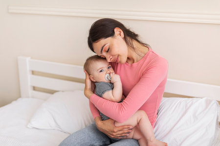 Portrait of loving mother resting with her infant baby girl in bed, woman holding daughter on hands...