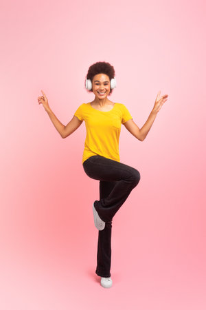 Smiling pretty young african american curly lady in wireless headphones dancing, enjoy musicの写真素材