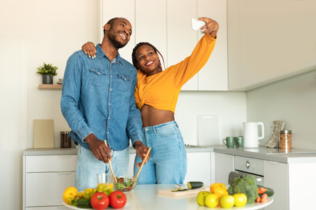 Happy black spouses making selfie while cooking together in kitchen at home, copy spaceの写真素材
