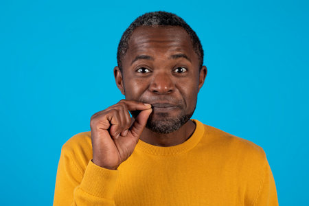 Black man showing mouth shut as zip with fingersの写真素材