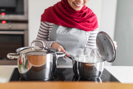 Unrecognizable muslim woman checking pot on stove, cooking at home