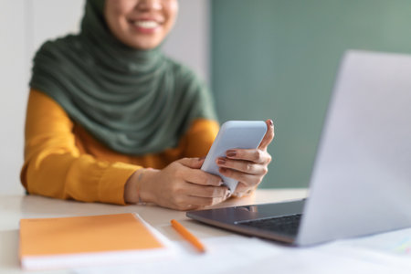 Muslim Woman In Hijab Using Mobile Phone While Sitting At Desk In Office